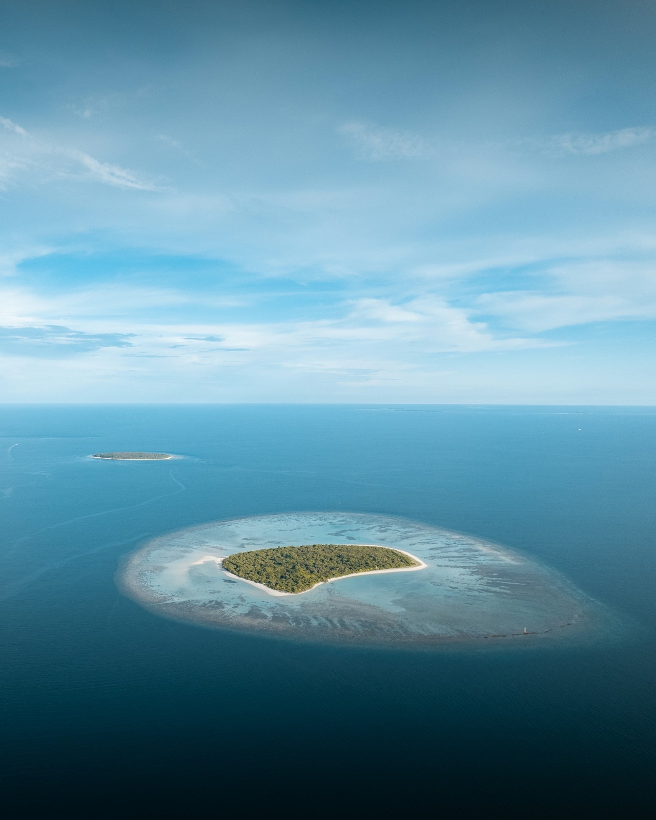 An aerial view of a green island and a turquoise lagoon in Noonu Atoll, Maldives.