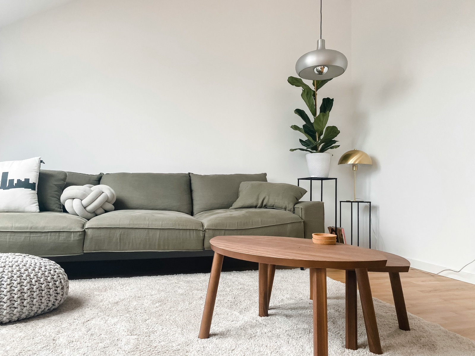 A gray sofa and nesting wooden tables in a light room with a plant and pendant lamp.